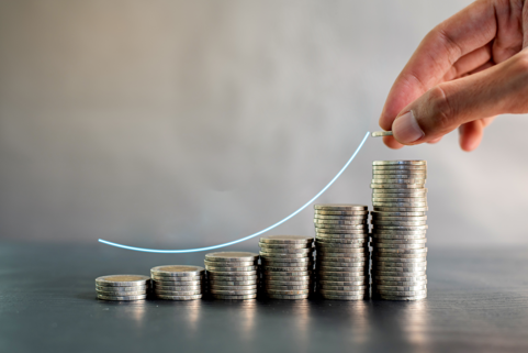 Stacks of coins are lined up from the smallest to the largest stack. A hand places a coin on the largest stack. A curved line follows the slope of the coin piles.