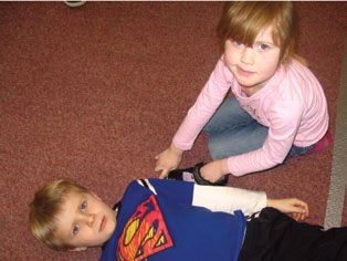 A student uses a shoe as a unit of measurement, to measure a friend who is lying down.