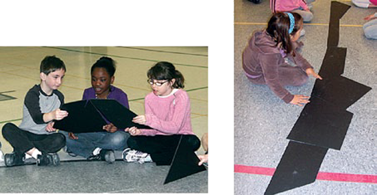 Students are sitting on the floor, manipulating large cardboard shapes.