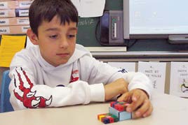 A student works with paper prisms and interlocking cube prisms.