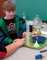 Students doing an experiment. They have as equipment: a funnel, water, a graduated cylinder, a tray.